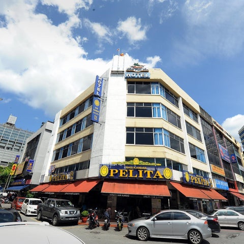 A multi-story hotel building with a prominent sign and storefronts sits on a busy street with parked cars and pedestrians.