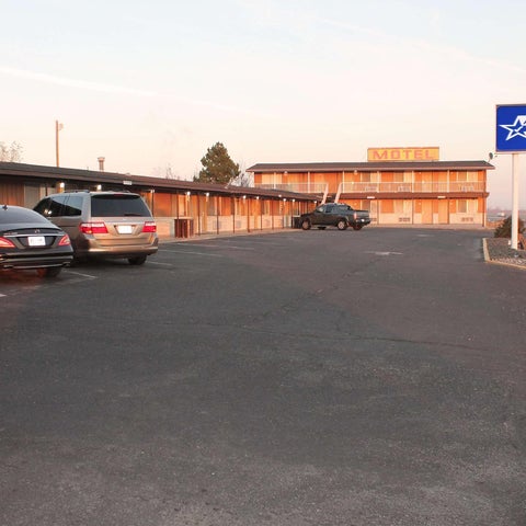 An Americas Best Value Inn motel is seen with several cars parked in front of it on a cloudy day.