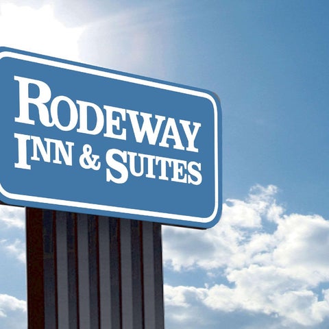A blue and white roadside sign for a Rodeway Inn & Suites stands against a partly cloudy sky.