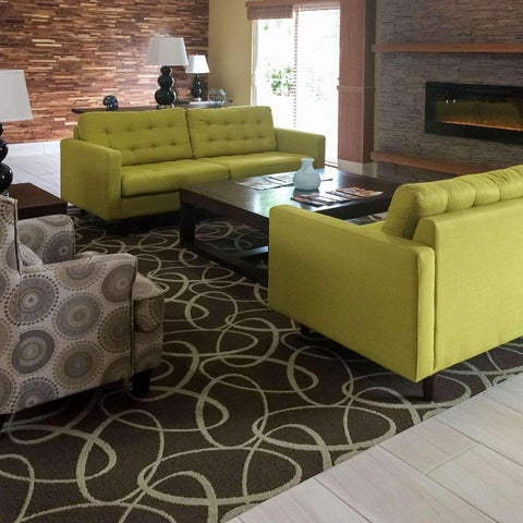 A lobby area features a patterned rug, a green sofa, and two armchairs arranged around a coffee table.