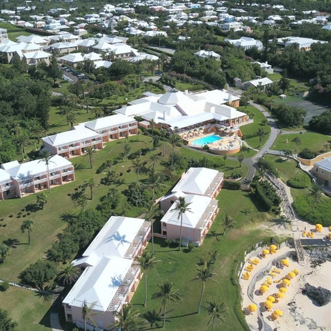 An aerial view showcases a sprawling resort complex with multiple buildings, a pool, and a beachfront location.