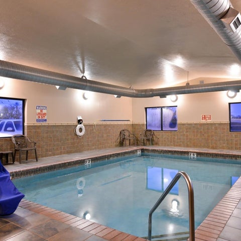 An indoor pool with a tiled edge and brick surround features two windows and chairs in a hotel setting.
