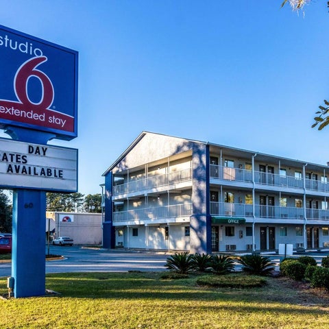 A studio 6 extended stay hotel features a blue sign and a multi-story building with balconies and a grassy front area.