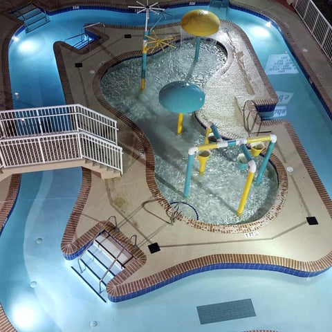 An aerial view shows a lazy river pool with a winding path, water features, and surrounding concrete decking.