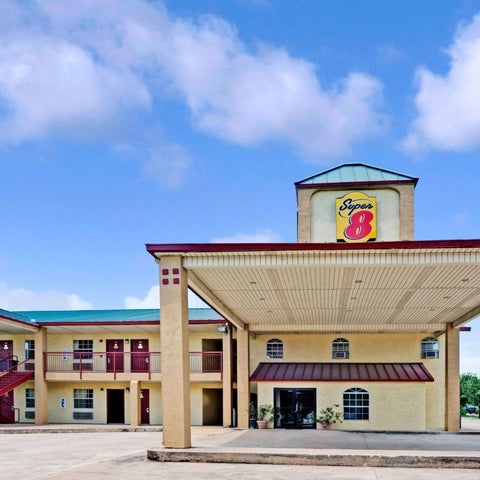 A Super 8 motel is shown with a red and beige facade, a covered entrance, and a cloudy blue sky in the background.