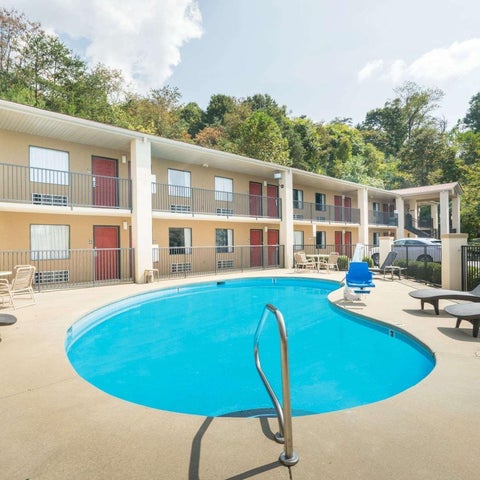 A kidney-shaped pool with lounge chairs and a patio area sits in front of a multi-story hotel.