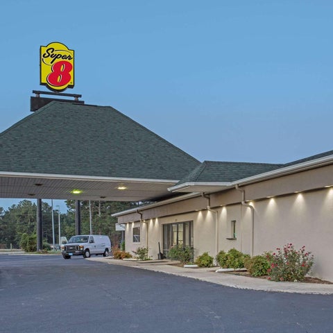 A Super 8 motel is shown with its sign, parking lot, and building facade under a partly cloudy sky.
