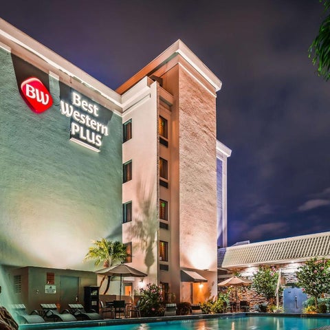 A Best Western Plus hotel building with a pool and patio area visible at night, featuring illuminated landscaping.