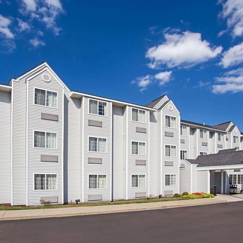 A multi-story white hotel building with a covered entrance and parking lot under a partly cloudy sky.