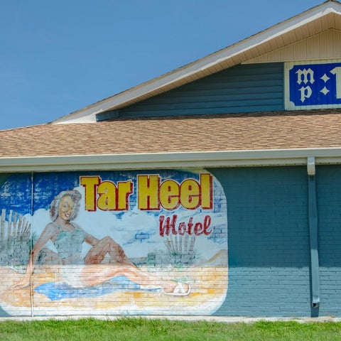 A motel with a large mural depicting a woman on a beach is shown against a clear blue sky.