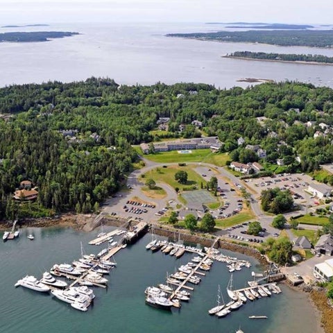 An aerial view shows a coastal town with a marina, residential areas, and lush green islands in the distance.