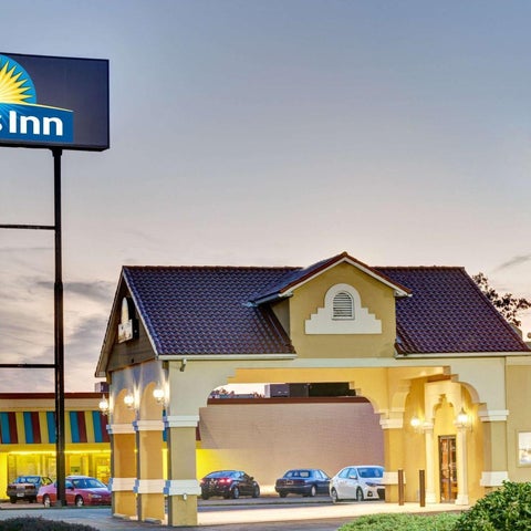 A Days Inn hotel building facade with a red tile roof and parking area is shown against a sunset sky.