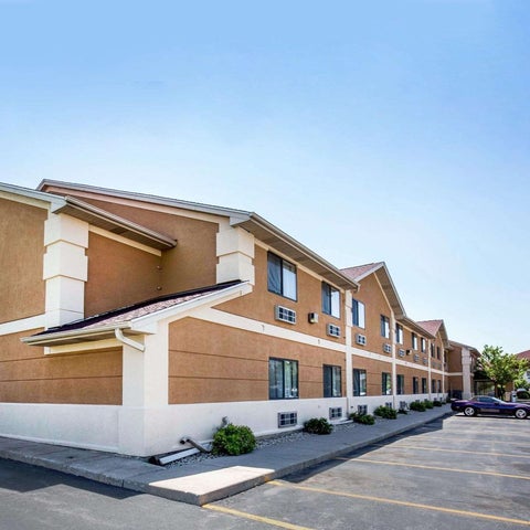 A Quality Inn hotel building facade with a sign, parking lot, and landscaping visible on a sunny day.