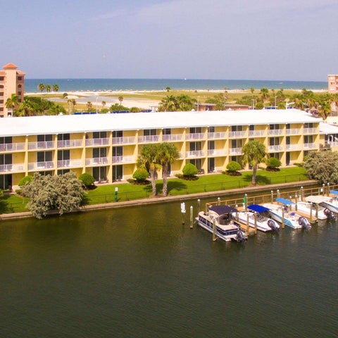 A multi-story hotel building sits on the edge of a waterway with boats docked and a beach visible in the background.