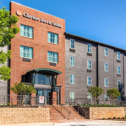 A brick building with a Clarion Inn & Suites sign features a multi-level entrance with stairs and landscaping.
