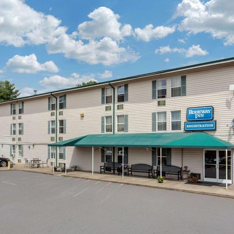 A two-story Rodeway Inn building with a covered entrance and parking area is shown under a partly cloudy sky.
