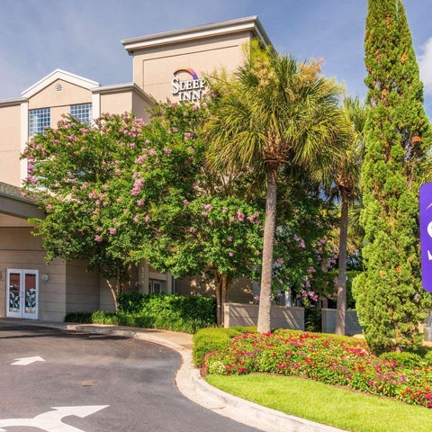 A Sleep Inn hotel is shown with a sign, landscaping, and palm trees in front of the building.