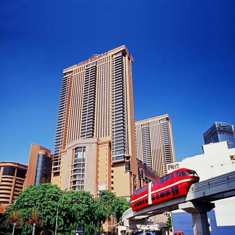 A high-rise hotel complex with a monorail passing in front, set against a clear blue sky.