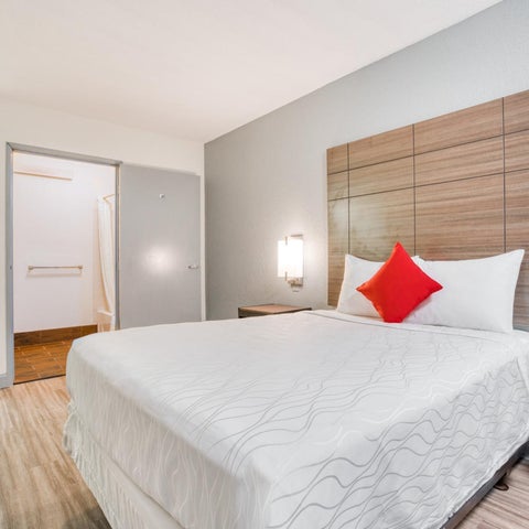 A hotel room features a king-sized bed with a decorative wood headboard and a view of a bathroom doorway.
