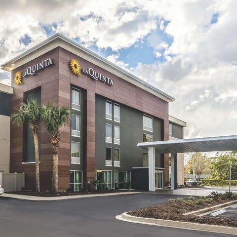 A La Quinta Inn & Suites building features a modern facade with palm trees, a covered entrance, and a parking lot.