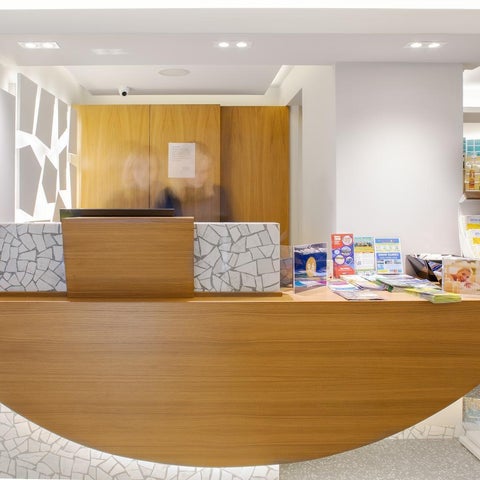 A modern hotel reception area features a curved wooden desk with brochures and a patterned front panel.