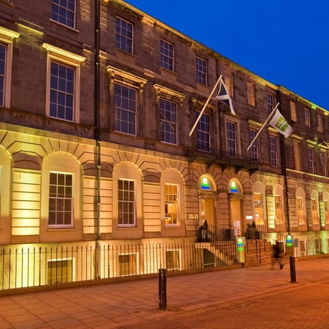 A grand, illuminated building with classical architecture features a prominent entrance and flags.