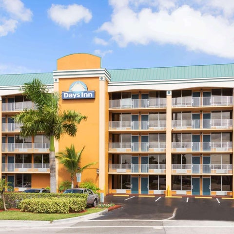 A multi-story Days Inn hotel features a light orange facade, balconies, and palm trees in front of the building.