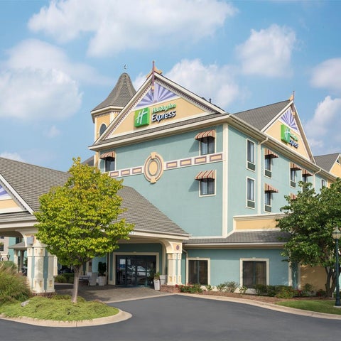 A multi-story Holiday Inn Express hotel building with a distinctive turret and covered entrance is shown under a partly cloudy sky.