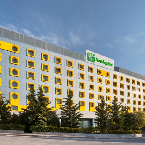 A large Holiday Inn hotel building with distinctive yellow circular windows and a green and yellow logo stands against a partly cloudy sky.