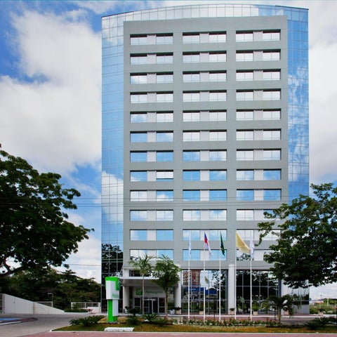 A tall, modern glass building with a landscaped entrance and flags displayed in front.