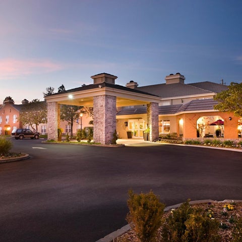 A large hotel building with a covered entrance and well-manicured landscaping is illuminated at dusk.