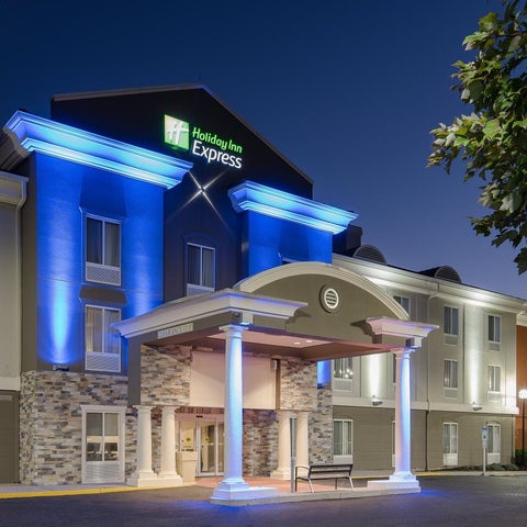 A brightly lit Holiday Inn Express hotel facade features a stone base, blue accents, and a covered entrance with columns.