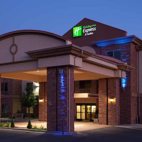 A Holiday Inn Express & Suites building facade is illuminated with blue lighting at dusk, showcasing its brick and stone architecture.