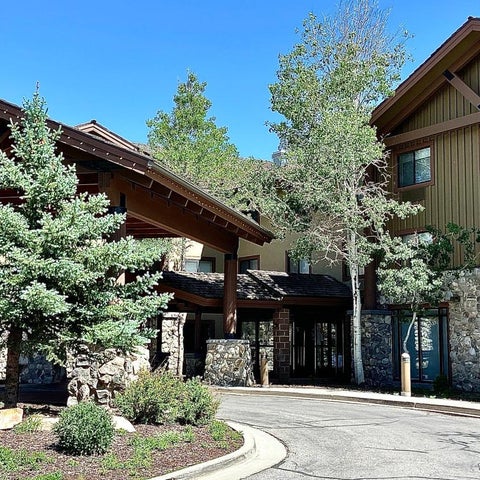A multi-story hotel building with a stone facade and exposed wood beams stands surrounded by lush greenery and trees.