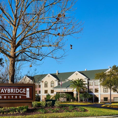 A Staybridge Suites hotel is shown with a sign, palm trees, and a multi-story building with a green roof.