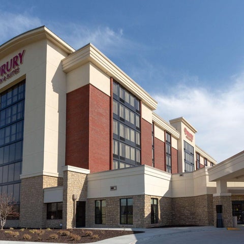 A Drury Hotel building features a tan and red brick facade with a covered parking area and a prominent logo.