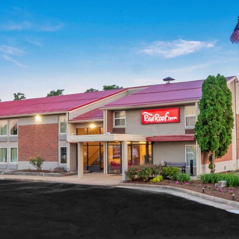A Red Roof Inn building with a red roof and a US flag, featuring a brick facade and landscaping.