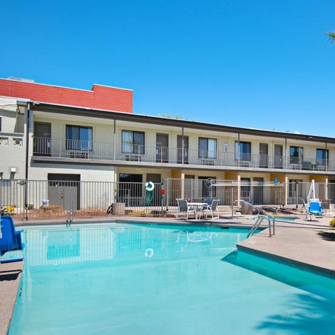 A bright blue pool with lounge chairs and a building with balconies sits under a clear blue sky.