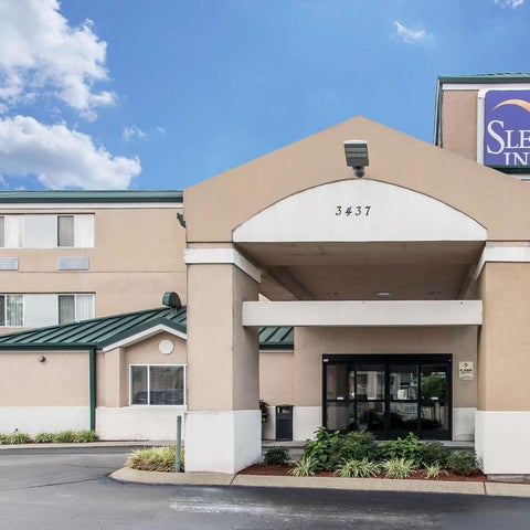 A Sleep Inn hotel building is shown with a covered entrance, landscaping, and signage against a partly cloudy sky.