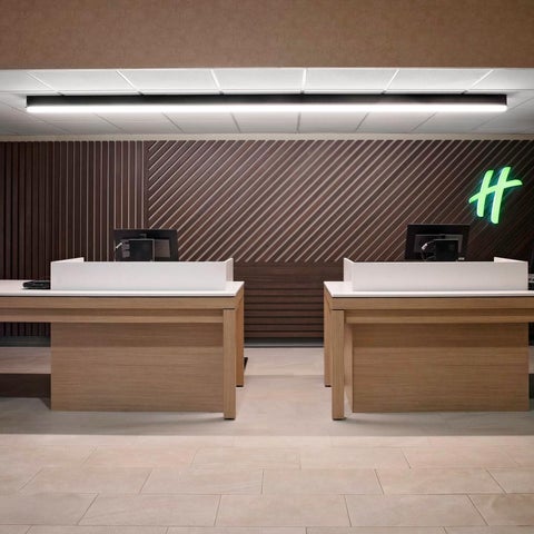 A modern hotel lobby features a long reception desk with wood accents and a backlit logo against a textured wall.