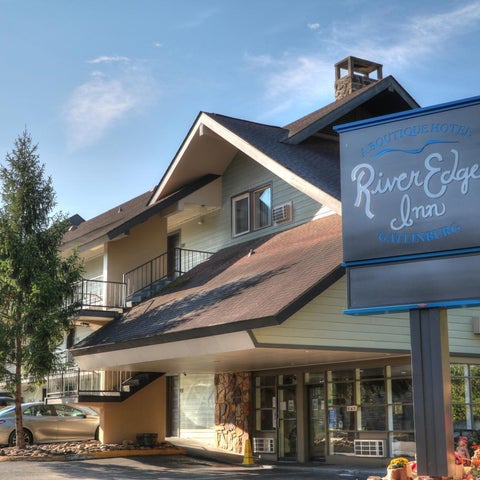 The River Edge Inn building facade features a brown roof, a blue sign, and a parking lot with several cars.