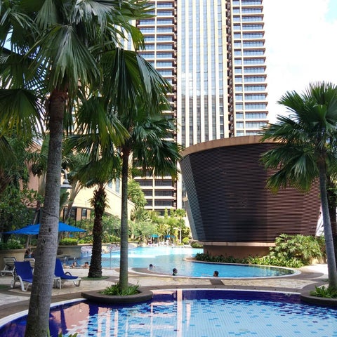 A bright blue pool with lounge chairs and palm trees sits in front of a large hotel building.