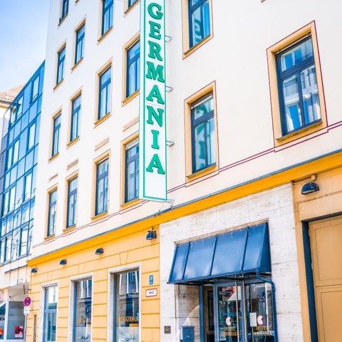 The Hotel Germania building facade features a prominent green sign, a covered entrance, and a silver car parked in front.