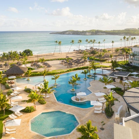 An aerial view showcases a luxury resort with a winding pool, beach, palm trees, and ocean views.
