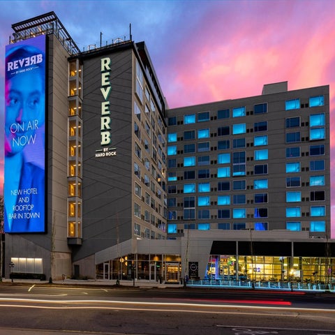 The Reverb hotel, by Hard Rock, is illuminated at dusk with a large digital display showcasing a person on air.