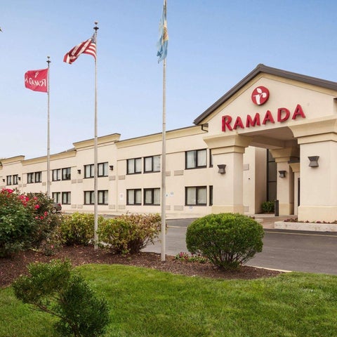A Ramada hotel building facade with flags and landscaping visible in front of the entrance.