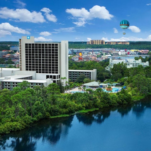 An aerial view showcases a large hotel complex with a pool, lake, and a hot air balloon floating above the landscape.