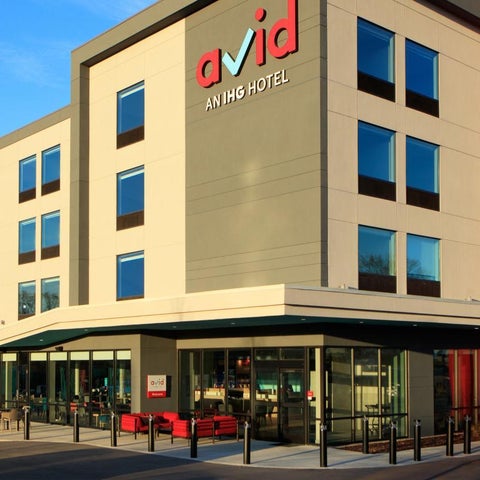 A modern hotel building with a red accent wall and a covered entrance with glass doors and a walkway.