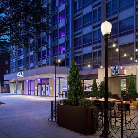 A modern hotel facade with outdoor seating, string lights, and landscaping is illuminated at dusk.