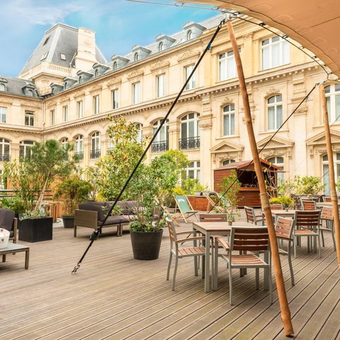 A rooftop terrace with outdoor seating and a view of a classic Parisian building with ornate architecture.